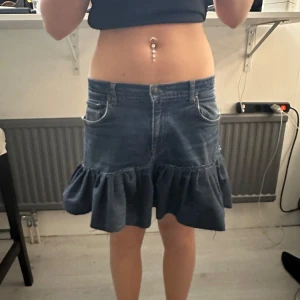 Jeanskjol med volang - Säljer en blå jeanskjol med volangkant nertill i storlek m men passar mig som brukar ha xs-s. Kjolen har klassiska jeansfickor fram och bak samt dragkedja och knapp i midjan. Perfekt för dig som gillar en trendig och avslappnad stil.