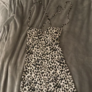 Leopardmönstrad klänning med smala axelband - Säljer en snygg leopardmönstrad klänning med smala axelband och markerad byst. Klänningen har en figurnära passform och är tillverkad i ett mjukt, glansigt material. Perfekt för dig som vill sticka ut med ett djurmönster.