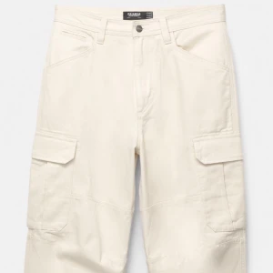 Beiga cargopants från Pull and Bear - Stilrena cargopants i beige med raka ben och stora fickor på sidorna. Byxorna har normal passform och är tillverkade i bomull. Klassisk design med knapp och dragkedja i midjan. Pris kan diskuteras 