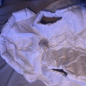 Moncler väst - Säljer en snygg vit dunväst från Moncler med huva och dragkedja. Västen har två fickor med dragkedja, den är använd max 3-4 gånger. Byten mot cardigan eller Loubs är av intresse.GÅR ATT KÖPA VIA PLICKS KÖPSKYDD!!!