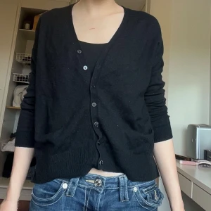 Svart kofta från Gina Tricot - Säljer en svart kofta från Gina Tricot med v-ringning och knappar framtill. Tröjan har lång ärm och är i mjukt material, perfekt att slänga över ett linne eller t-shirt. Enkel och stilren modell som passar till det mesta.