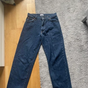 Mörkblå jeans från Woodbird - Säljer ett par klassiska mörkblå jeans från Woodbird med raka ben och femficksdesign. Jeansen har normal passform, knappgylf och läderpatch med logga bak i midjan. Perfekta till vardags för en stilren look.