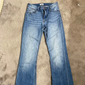 Blå bootcut jeans från Lindex - Säljer ett par klassiska blå bootcut jeans från Lindex. Jeansen har normal passform, fem fickor och stängs med dragkedja och knapp. Storlek 38, sparsamt använda!