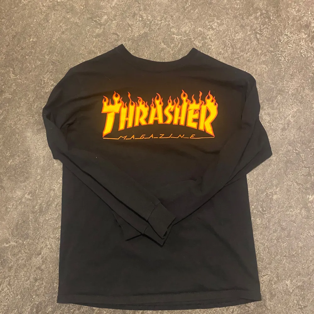 Säljer en svart långärmad tröja från Thrasher med den klassiska loggan i eldigt gult och orange framtill. Perfekt för dig som gillar streetwear och skate. Mjuk bomullskvalitet och normal passform.. Paidat.