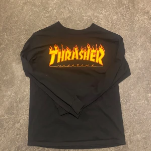Svart långärmad Thrasher-tröja - Säljer en svart långärmad tröja från Thrasher med den klassiska loggan i eldigt gult och orange framtill. Perfekt för dig som gillar streetwear och skate. Mjuk bomullskvalitet och normal passform.