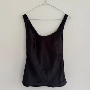 Svart linnetopp från ASOS DESIGN - Säljer en stilren svart linnetopp från ASOS DESIGN. Toppen har djup urringning både fram och bak, är ärmlös och har en slät, lätt glansig satin yta. Perfekt att matcha med allt!