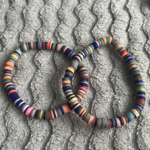 Färgglada armband med platta pärlor - Två elastiska armband med platta, färgglada pärlor i olika nyanser av blått, orange, rosa, grönt och grått. Perfekta för att addera lite färg till din stil.