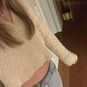 Beige fluffig croppad tröja - Mysig croppad tröja i beige med fluffig textur och v-ringad hals. Långärmad modell som passar perfekt till jeans eller kjol. Enkel och stilren design utan synliga detaljer eller mönster.