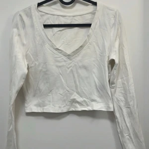 Vit croppad långärmad topp med v-ringning - Säljer en enkel och stilren vit croppad topp med lång ärm och djup v-ringning. Perfekt att matcha med jeans eller kjol för en clean look. Toppen är i mjuk bomull och passar till många olika outfits.