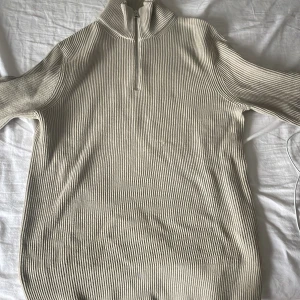 Beige ribbad stickad halvzip från Jacquemus - Säljer en beige ribbad stickad tröja från Jacquemus med halv dragkedja och hög krage. Perfekt för lager-på-lager och har en stilren, minimalistisk look. Passar både till jeans och kjol.