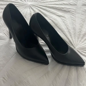 Svarta pumps från Rodebjer - Säljer ett par klassiska svarta pumps från Rodebjer med spetsig tå och hög klack. Skorna är tillverkade i skinn och har en elegant och tidlös design som passar till många olika outfits. Helt nya och oanvända, har dock ingen originalföråsckning kvar. Säljes pga fel storlek på mig. Nypris: 3000kr