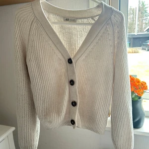 Vit stickad kofta  - Säljer en vit stickad kofta från H&M med v-ringning och stora svarta knappar framtill. Litet hål vid armen där bak men inget som märks. Storlek 158/164, passar S 💝