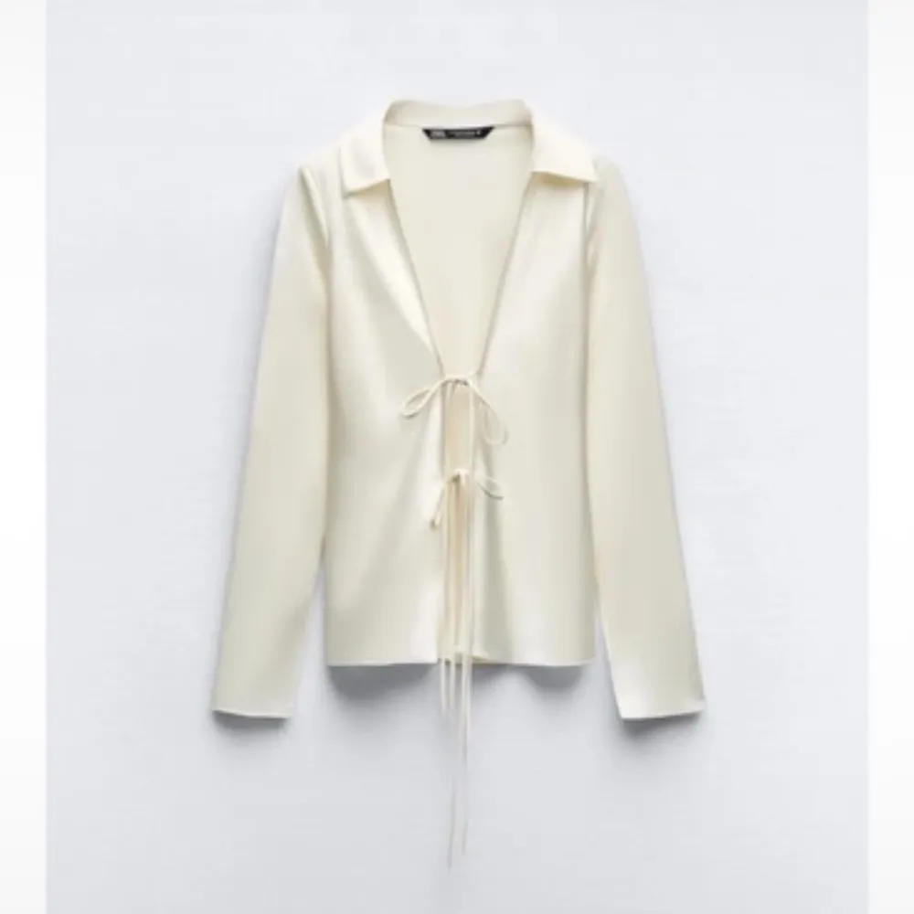 Snygg vit blus i satin från Zara med lång ärm och djup v-ringning. Blusen har knytning framtill och en klassisk krage. Perfekt för att skapa en stilren och trendig look.. Yläosat.