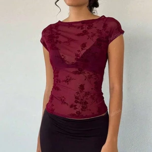 🍷🍇 mesh Topp - Säljer en vinröd mesh topp med blommigt mönster och korta ärmar. Toppen är tight och har en transparent look som ger en trendig vibe. Perfekt att styla med kjol eller jeans för en cool outfit.