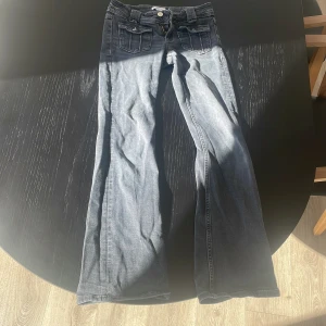 Grå jeansbyxor från Gina Tricot - Säljer ett par grå jeansbyxor från Gina Tricot i storlek 152. Byxorna har raka ben, fickor med lock och knapp framtill samt klassisk dragkedja. Perfekta för dig som gillar en avslappnad och tidlös stil.