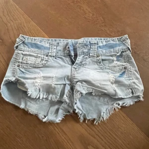 Lågmidjade ljusblå jeansshorts  - Säljer ett par lågmidjade ljusblå jeansshorts från Fishbone i storlek XS. Shortsen har slitna detaljer, fransig kant och klassisk femficksmodell. Skriv för fler bilder, pris kan diskuteras! Midjemåttet tvärs över midjan är ungefär 37cm💓