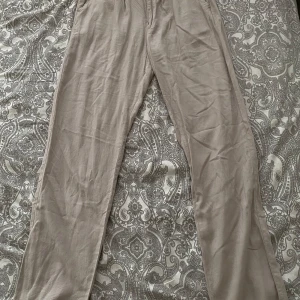 Beige linnebyxor från Lager 157 - Säljer ett par ljusbeige linnebyxor från lager 157 med normal passform. Byxorna har hällor för bälte, knapp och dragkedja framtill samt sidfickor. Perfekta för varmare dagar och en avslappnad stil.