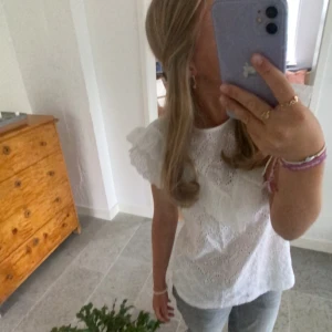 Vit blus med volang och broderade detaljer - Säljer en söt vit blus med volang över axlarna och broderade hålmönster. 