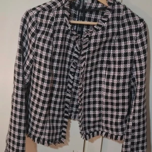 Rutig kavaj från H&M Divided - Säljer en snygg rutig kavaj i svart, vit och rosa från H&M Divided. Jackan har fransiga kanter och är i ett mjukt, vävt material. Perfekt för att lyfta en outfit med lite extra stil.