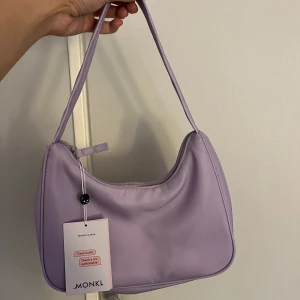 Lila axelväska från Monki - Säljer en lila axelväska från Monki. Aldrig använd med prislapp kvar. Köptes för 180 kr 