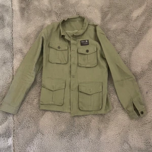 Grön overshirt (S) - Säljer min gröna overshirt med fyra stora fickor framtill och knappar längs hela framsidan. Jackan har klassisk krage och långa ärmar med knapp vid ärmslut. Perfekt att styla lager på lager. Perfekt nu till våren 