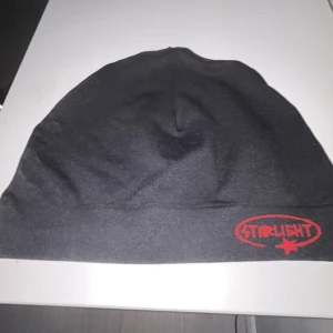 Svart mössa med röd Starlight-logga - Svart mössa med röd Starlight- framtill. den är bara använd 2-3 gånger. Enkel och stilren design, perfekt för att hålla värmen under kyliga dagar. Mjuk och bekväm passform.