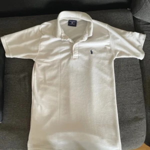 Vit pikétröja från Polo Sport - Klassisk vit pikétröja från Polo Sport i 100% bomull. Tröjan har korta ärmar, krage och knappar framtill samt den ikoniska broderade loggan på bröstet. Perfekt för en clean och sportig stil.