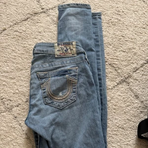 Ljusblå skinny jeans från True Religion - Säljer ett par ljusblå skinny jeans från True Religion med klassiska detaljer och snygga sömmar på bakfickorna. Jeansen har normal passform i midjan och är tillverkade i mjukt denimtyg. Perfekta för dig som gillar en smal siluett.