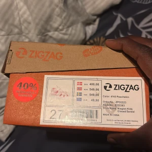 Glittriga peachfärgade sandaler från Zigzag - Säljer ett par glittriga peachfärgade sandaler från Zigzag för barn. Skorna har stängd tå, vit platt sula och kardborreband med logga. Perfekta för sommaren med snyggt glittrande material och sportig design.