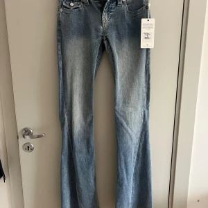 NYA! Blå flare jeans från True Religion lowrise - Säljer ett par NYA lowrise klassiska flare jeans från True Religion med snygga detaljerade bakfickor och silverfärgade knappar. Jeansen har en lätt tvättad look och normal passform. Perfekta för dig som gillar en tidlös stil med lite edge.