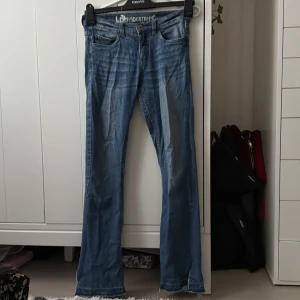 Blå bootcut jeans från L8 Industries - Säljer ett par klassiska lågmidjade bootcut jeans från L8 Industries. Jeansen har normal passform, fem fickor och hällor för bälte. Perfekta för dig som gillar en tidlös denimlook med lite utsvängda ben. Storlek: 158 barn storlek men kan passa xxs.