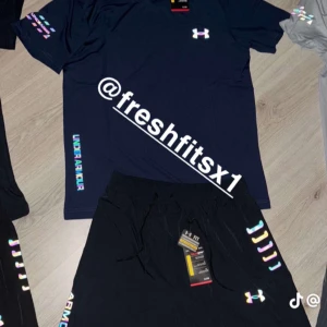 Mörkblå set från Under Armour - Mörkblå set från Under Armour med logga på bröstet och färgglada detaljer på ärmen samt texten UNDER ARMOUR längs sidan. Perfekt för träning eller sportiga tillfällen. 