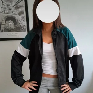 Rotation svart och turkos träningsjacka - Snygg oversized träningsjacka från Rotation i storlek Large. Jackan är svart med turkosa axelpartier och vita detaljer på ärmarna. Dragkedja framtill, ståkrage och två fickor med dragkedja. Köpt på Carlings. Använd fåtal gånger.