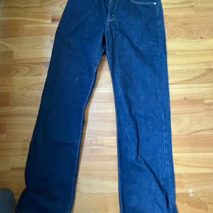 Levi's blå jeans W33 L32 - Klassiska mörkblå jeans från Levi's i rak modell. Jeansen har fyra fickor, tydliga kontrastsömmar och patch bak i midjan. Tillverkade i slitstarkt denimtyg, perfekta för en avslappnad och tidlös stil.