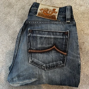 Blå jeans från Jacob Cohën - Skick: 8/10, lappad men ser ut som design - Storlek: 30- Längd:90cm Midja:37cm ben:16cm - Nypris: 5000 kr+
