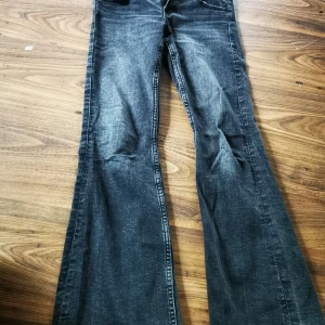 Bootcut jeans från Gina Tricot, svarta - Snygga svarta bootcut jeans från Gina Tricot i storlek 152. Jeansen har klassisk femficksdesign, coola bakfickor med lock och knappar samt en tvättad look. Perfekta för dig som gillar retrovibbar och vill ha ett par jeans med lite extra attityd.