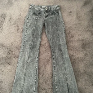 Grå bootcut jeans från Nelly - Säljer ett par grå bootcut jeans från Nelly med tvättad look. Byxorna har fram- och bakfickor samt dragkedja och knapp framtill. Perfekta för dig som gillar en retrostil med utsvängda ben.