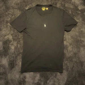 Svart t-shirt från Polo Ralph Lauren - Svart t-shirt från Polo Ralph Lauren med klassisk broderad logga på bröstet. Modellen är custom slim fit och har rund halsringning samt korta ärmar. Perfekt för en stilren och enkel look.