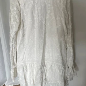 Vit spetsklänning från NA-KD - Superfin vit klänning från NA-KD med knytning i ryggen. Klänningen har långa ärmar, volang nertill och är dekorerad med broderade spetsdetaljer. Perfekt för sommarens tillfällen eller student🤍🤍