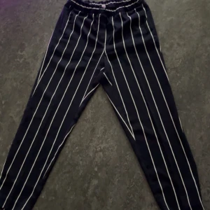 Mörkblå randiga byxor från H&M - Säljer ett par mörkblå byxor med vita vertikala ränder från H&M. Byxorna har resår i midjan och är i en lätt och bekväm modell. Perfekta för en stilren och avslappnad look.
