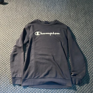 Blå sweatshirt från Champion - Säljer en blå sweatshirt från Champion med klassisk logga tryckt på bröstet. Tröjan har rund halsringning och långa ärmar. Storlek 160-166 och passar till det mesta. 