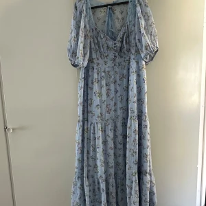 Ljusblå blommig långklänning från ASOS DESIGN - Superfin ljusblå långklänning från ASOS DESIGN med blommigt mönster och puffärmar. Klänningen har v-ringning, volangdetaljer och knytning i ryggen. Perfekt för sommarens alla tillfällen!