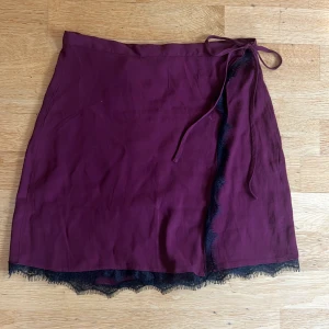 Vinröd omlottkjol med spetskant - Omlottkjol i en såååå snygg vinröd färg med svart spetskant och knytband i midjan. Kjolen är kort och har en ”dark feminin” vibe med mjukt, lätt tyg som faller fint. Knappt använd. Perfekt för varma sommar nätter. 🌃              bara skriv om du undrar något ! 💕