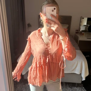 Persikofärgad blus med volangdetaljer - Säljer en persikofärgad blus från Zara med volanger och knytband vid ärmsluten. Blusen har v-ringning och är tillverkad i ett lätt, skrynkligt material. Perfekt för vår och sommar!💞