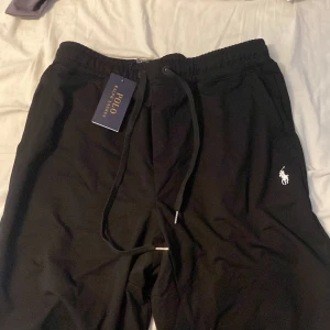 Svarta Polo Ralph Lauren shorts - Svarta mjukisbyxor från Polo Ralph Lauren med dragsko i midjan och broderad vit logga på benet. Byxorna har en avslappnad passform och är perfekta för en chill stil. Klassisk design med bekvämt material.