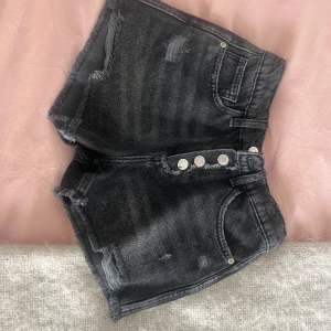 Svarta jeansshorts från Zara - Aldrig använda, fast lappen är borta. Snygga svarta jeansshorts från Zara med hög midja och slitna detaljer. Shortsen har råa kanter, flera knappar framtill och klassiska fickor både fram och bak. Perfekta för en chill sommarlook.