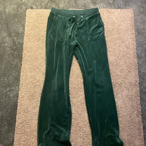 Mörkgröna velourbyxor Juicy Couture - Mörkgröna mjukisbyxor från Juicy Couture i mjuk velour med snörning i midjan och fickor både fram och bak. Byxorna har raka ben och snygga metalldetaljer med logga. Perfekta för en chill och trendig look. Priset kan diskuteras 