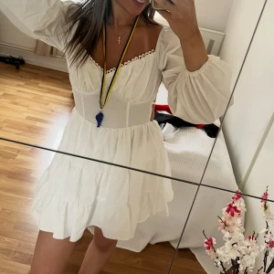 Vit kort klänning med puffärmar - Supersöt vit kort klänning med volanger och puffiga långärmar. Klänningen har öppen rygg med knyt och en söt kant vid urringningen. Perfekt för en studentklänning, själv hade jag den på mig när jag tog studenten och endast använt 2 timmar.