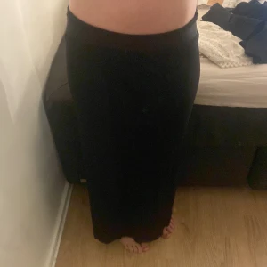 Svart långkjol med slits - Säljer en svart långkjol med slits på sidan. Kjolen har en enkel och stilren design som sitter snyggt i midjan och faller rakt ner. Perfekt för dig som gillar en klassisk look med en twist. Passar till många olika stilar och är lätt att matcha.