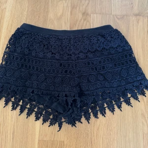 Svarta virkade shorts med spetsdetaljer - Säljer ett par svarta shorts med snygga virkade spetsdetaljer och fransar längst ner. 